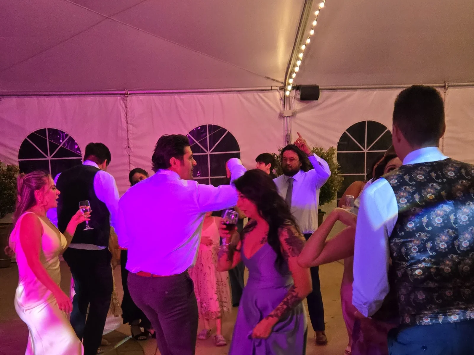 Wedding guests dancing under pink uplighting in a tented reception